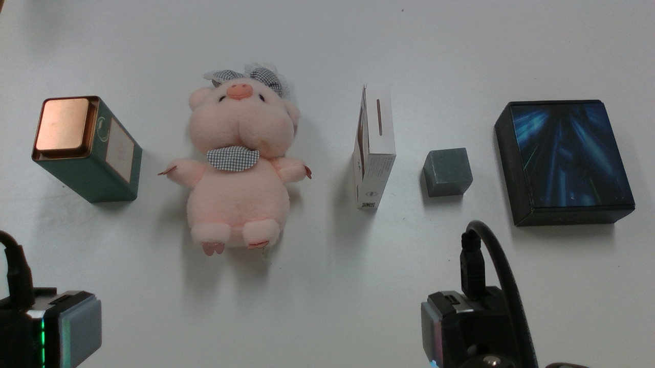 Initial scene: a plush pig, a metal tin, and three objects on the right: a white box, a grey cube and a black box